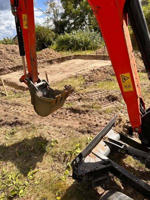 Wykop pod fundament wykonany minikoparką na działce za domem, widok na łyżkę i ramię maszyny.